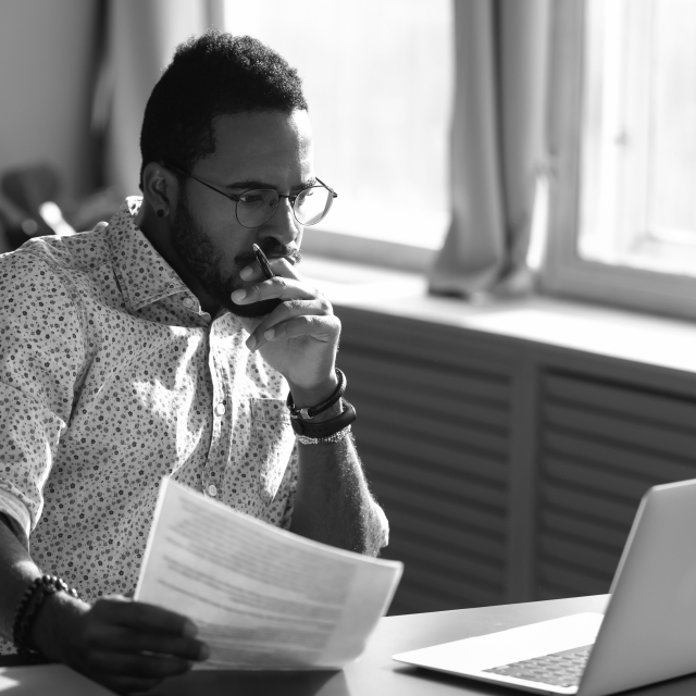 man looking at a printed document and his laptop